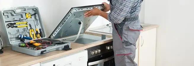Cooktop repair technician lifting a built-in stovetop for service in Charlotte, NC