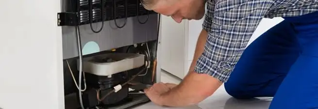 Refrigerator repair technician servicing the compressor and condenser area in Charlotte, NC
