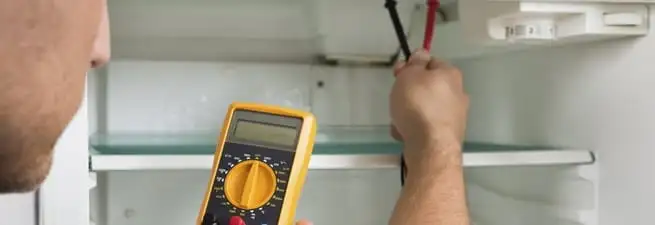 Refrigerator repair technician testing electrical components with a multimeter in Charlotte, NC
